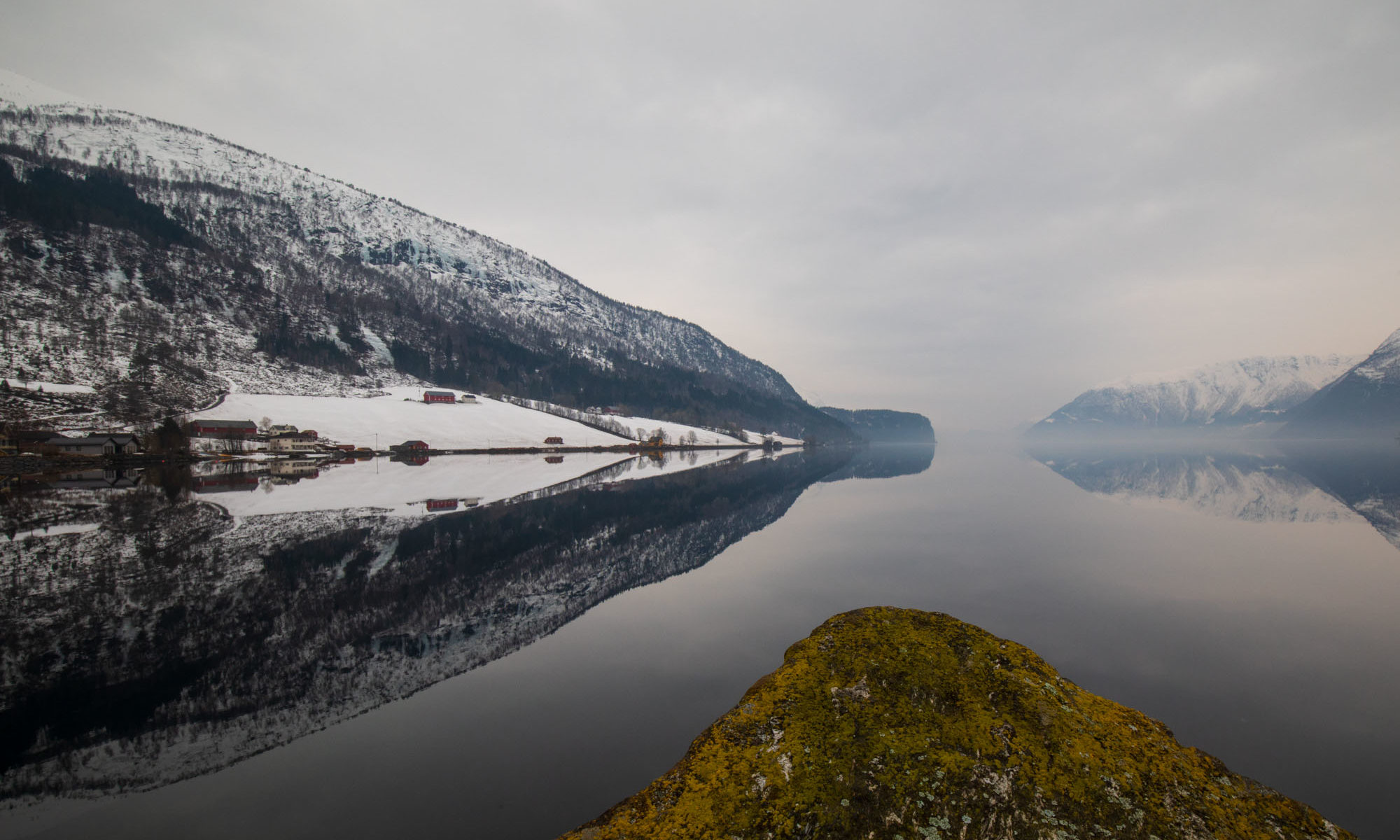 Mehrere schneebedeckte Berge spiegeln sich im Fjord.