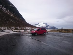 Bild eines roten Campervans auf einem leeren Parkplatz.