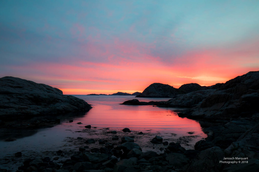 Foto von Wasser und Steinen mit einem rot-gelben Sonnenuntergang am Südkapp in Norwegen.